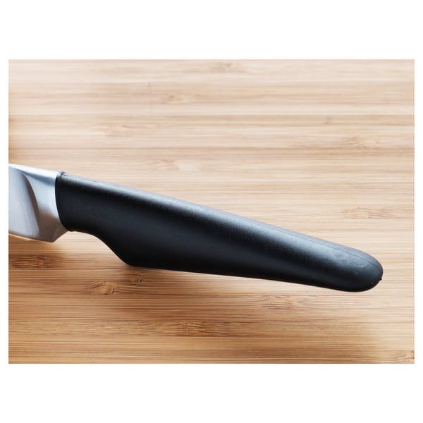 Couteau d’office à manche noir sur une planche à découper en bois, mettant en valeur sa lame élégante et tranchante et sa prise en main ergonomique.