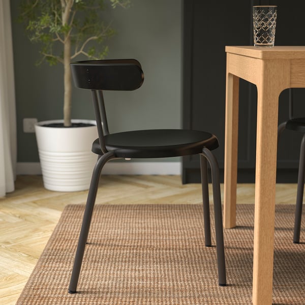 Chaise noire moderne avec dossier arrondi, parfaite pour manger. S’empile ou s’accroche facilement à la table pour un gain de place.