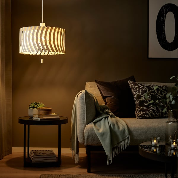 Salon confortable avec lampe YTLÄGE, abat-jour marron, canapé gris, oreillers verts et plante.