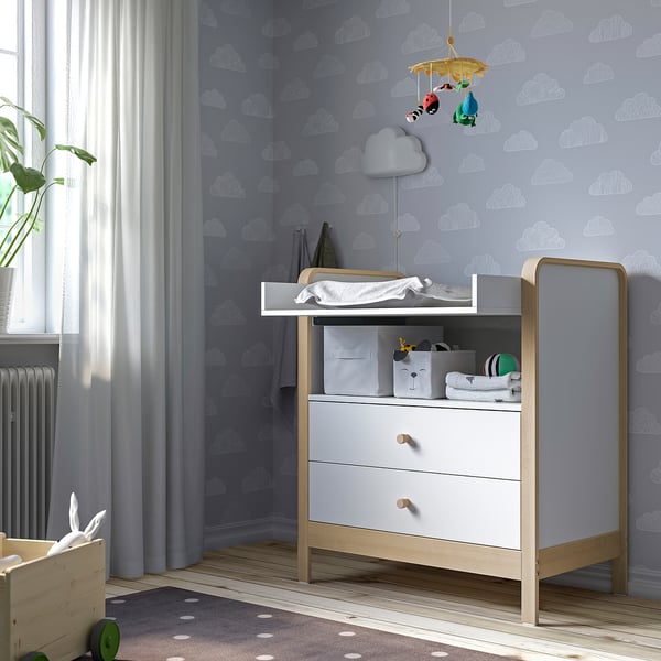 Grijs dressoir voor de kinderkamer met 3 lades, aankleedkussen, verrijdbaar, plant, blauw behang, vloerkleed.