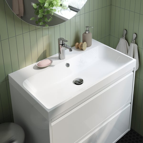 Moderne witte badkamermeubel met een enkele strakke wastafel en chromen armaturen, geplaatst tegen groene tegelmuren.