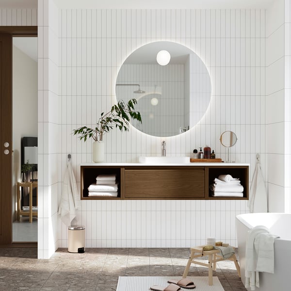 Moderne badkamer met ronde spiegel, houten wastafel, witte wastafel en een klein krukje met handdoeken.