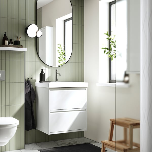 Moderne witte badkamer met ÄNGSJÖN wandkast, strakke handvatten, keramische wastafel, ronde spiegel, raam en houten kruk.