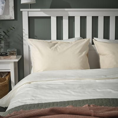 Beige ÄNGSLILJA katoenen kussenslopen op bed met wit hoofdeinde, dekbed, bruine plaid.