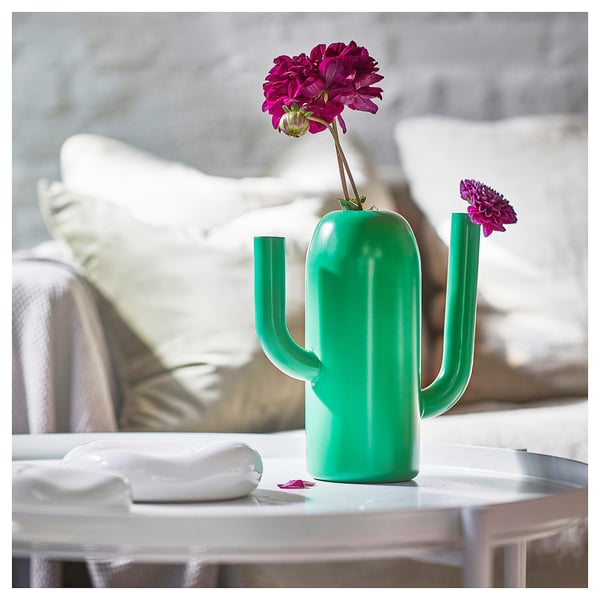 Heldergroene cactusvormige gietervaas met roze bloemen op tafel, modern design.