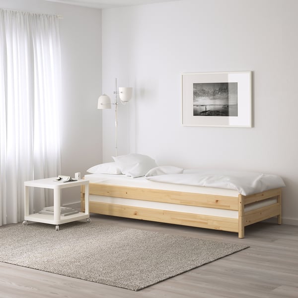 Moderne slaapkamer met ÅFJÄLL witte matras op eenvoudig houten bed, kleine witte tafel, grijs vloerkleed en kunst aan de muur.