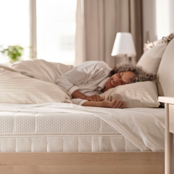 Een persoon die slaapt op een witte ÅKREHAMN-matras, klassiek ontworpen met een lamp ernaast.