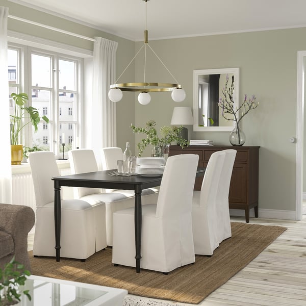 Moderne eetkamer met messing hanglamp, glazen bollen, witte stoelen, groene muur, planten, houten vloer.