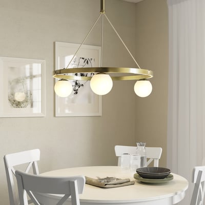 Messing hanglamp met drie glazen bollen boven de eettafel, die warm licht uitstraalt.