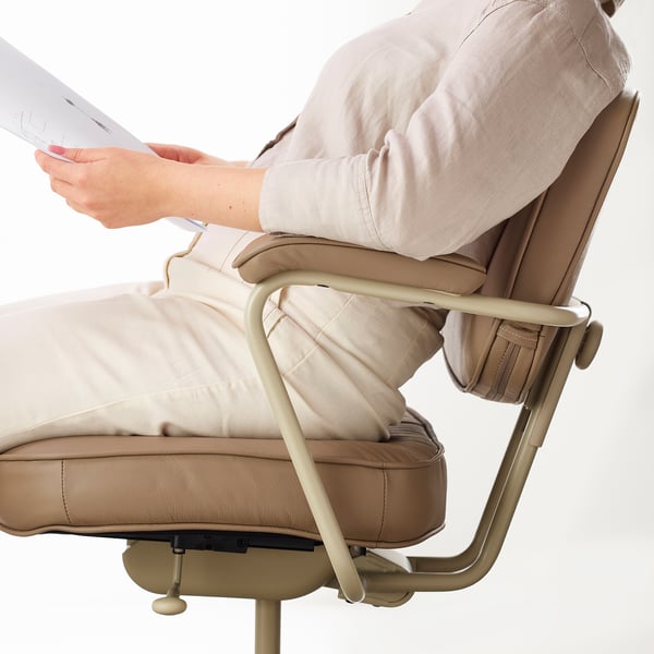 Een persoon past de lendensteun aan op een beige ALEFJÄLL-bureaustoel, afgebeeld met armleuningen en een goudkleurig metalen onderstel.