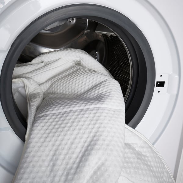 Witte wasmachine met grote, getextureerde witte deken erin, klaar om schoon te maken.