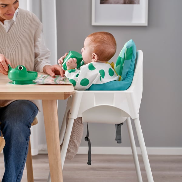 Baby in ANTILOP kinderstoel eet van kikkerkom als vrouw helpt.