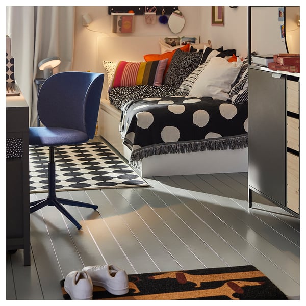 Moderne slaapkamer met zwart-wit beddengoed, kleurrijke kussens, blauwe stoel en tapijt met patroon.