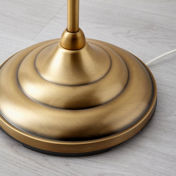 Goudkleurige metalen lampvoet op houten ondergrond. Getoond in close-up, met de nadruk op een strak ontwerp en hoogwaardige afwerking.