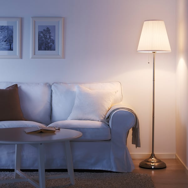 Gezellige woonkamer met lichtblauwe ÅRSTID lamp, witte kap, die zacht licht geeft in de buurt van een lichtblauwe bank en salontafel.