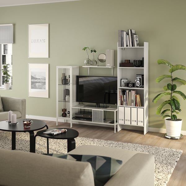 Witte BAGGEBO-kasten in groene woonkamer: tv-meubel, planken, kast. Beige bank, zwarte tafels, planten, boeken, kaarsen.