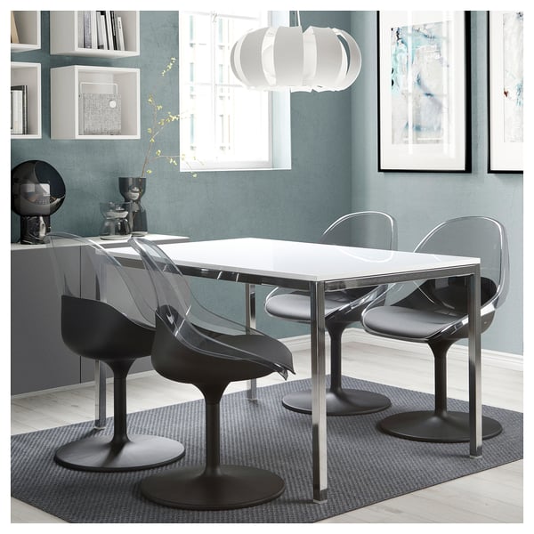 Moderne eethoek met witte tafel en vier zwarte BALTSAR draaistoelen. Strak, gebogen ontwerp, geplaatst onder een hanglamp, tegen een groenblauwe muur.
