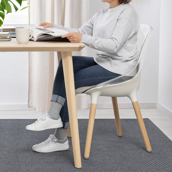 Persoon die aan tafel zit te lezen, met behulp van de BALTSAR-stoel. Stoel heeft transparante zitting, stevige beukenhouten poten en komvormige zitting.