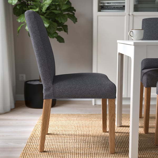 Grijze gestoffeerde stoel met houten poten in de buurt van witte tafel.