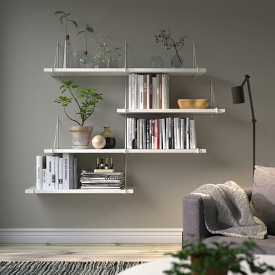 Moderne woonkamer: witte BERGSHULT planken met boeken, vazen, planten. Grijze muur, bank, lamp.