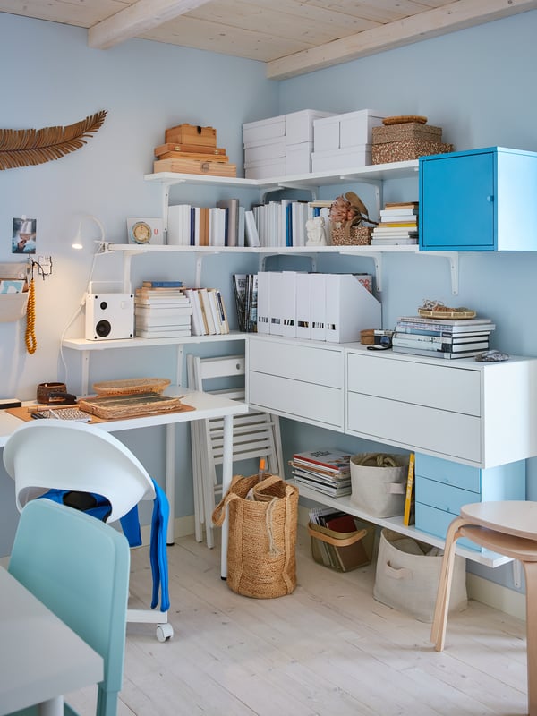 Helderblauw kantoor met witte planken, boeken, manden en dozen. Lichte houten vloeren en plafondbalken versterken het luchtige gevoel.