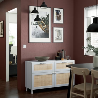 Stijlvolle eethoek met wit en rotan dressoir, marmeren schaal, hanglampen en kunstwerken. Het is een prominent stuk tegen de bordeauxrode muur.