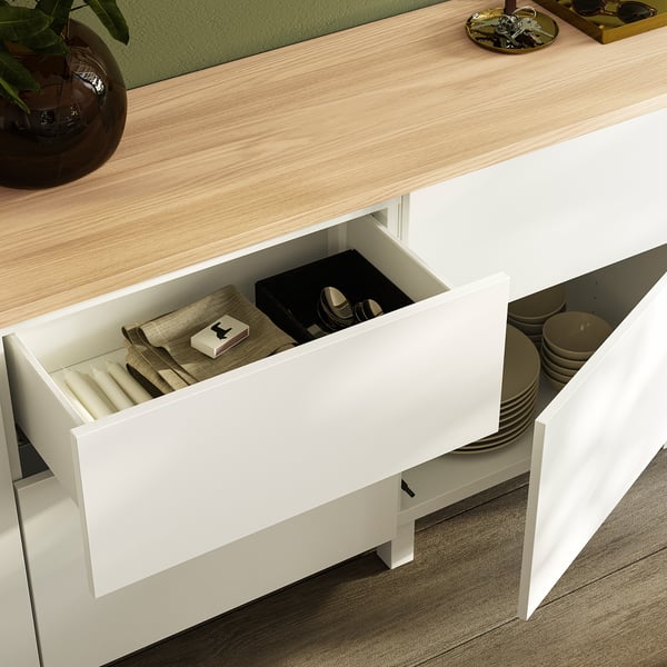 Witte BESTÅ-lade open, waaruit georganiseerd bestek, borden en servetten zichtbaar werden. Moderne keukenopslag.