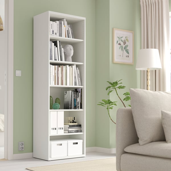 Moderne woonkamer met BESTÅ boekenplank en inrichting. Hoge, smalle, verstelbare plank. Beige fauteuil & lamp ernaast.