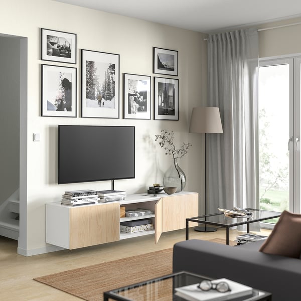 Moderne woonkamer met wit BESTÅ tv-meubel, flatscreen tv en zwarte salontafel. Versierd met zwart-wit foto's en een hoge lamp.