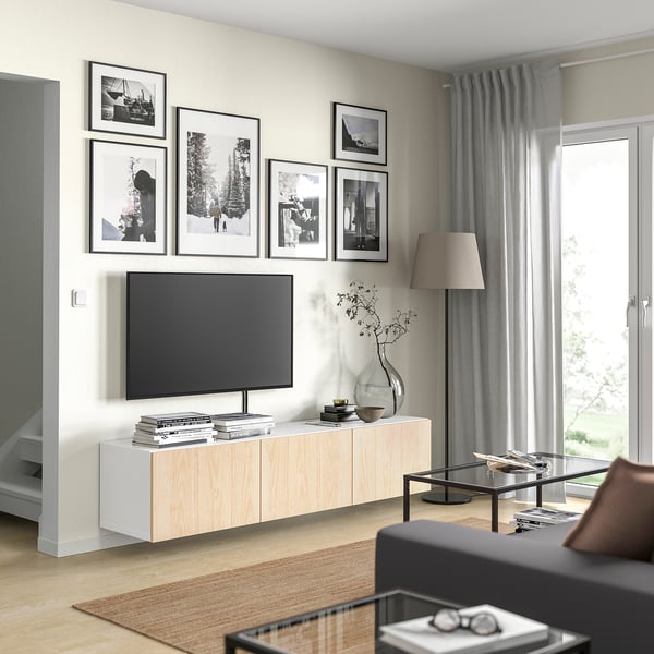 Moderne woonkamer met lichthouten tv-meubel, zwarte tv, ingelijste foto's, grijze gordijnen en zwarte bank.