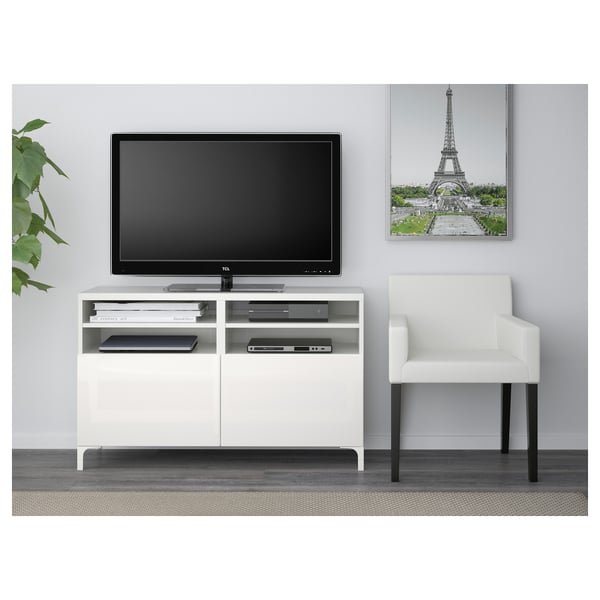 Witte tv-standaard met open planken, waarin een flatscreen-tv is ondergebracht. Het biedt kabelbeheer en opslag, met een stoel ernaast.