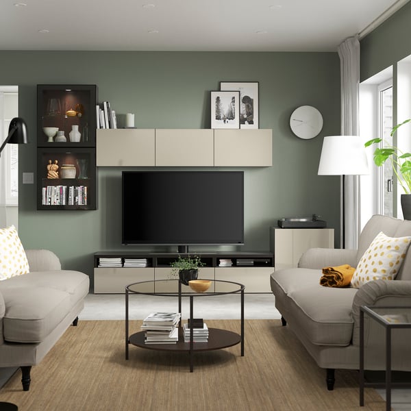 Moderne woonkamer met BESTÅ tv-meubel, neutrale kleuren, groene muren, houten vloer, twee banken met polkadotkussens, een ronde tafel en een hoge lamp.