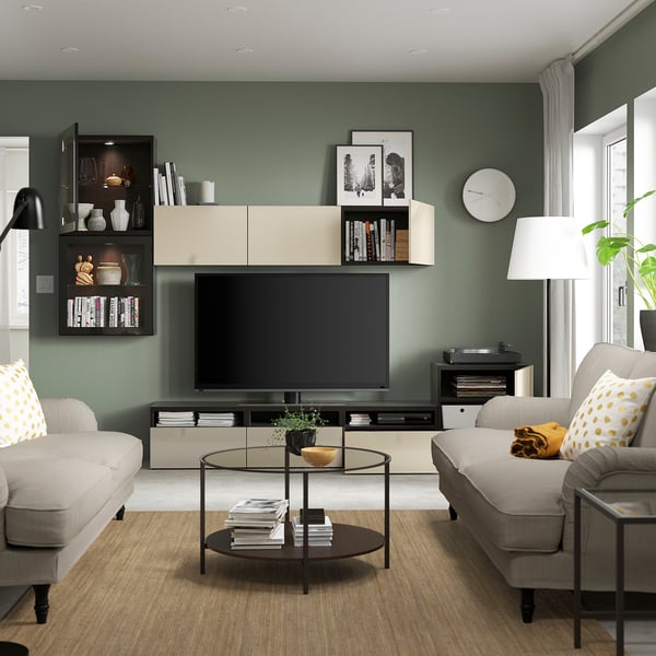 Moderne woonkamer met groene muren. Grijze banken, houten salontafel, grote tv op opbergmeubel, versierde planken en een ronde wandklok.