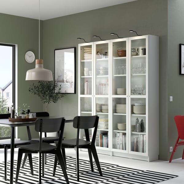 Moderne eetkamer met BILLY witte boekenkasten met glazen deur, zwarte stoelen, groene muren, gestreept vloerkleed en hanglamp.