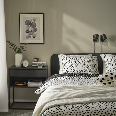 Stijlvolle slaapkamer met BJÖRKGRÅMAL dekbed, plant, boeken en lampen.