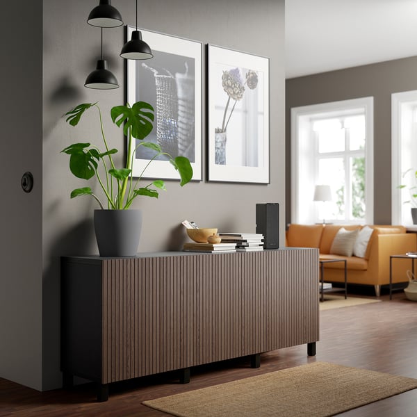 Donker eiken BJÖRKÖVIKEN dressoir met plant en boeken. Oranje banken, foto's en lampen.