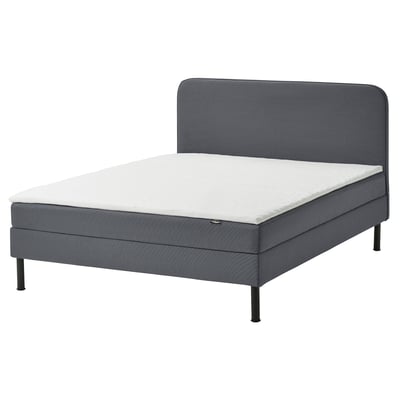 Grijs modern boxspring bed met gewatteerd hoofdeinde en witte matras.
