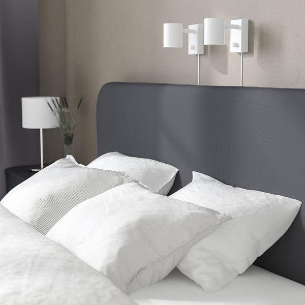 Modern bed met gewatteerd hoofdeinde, schoon wit linnengoed en wandlampen, die comfort en stijl bieden.
