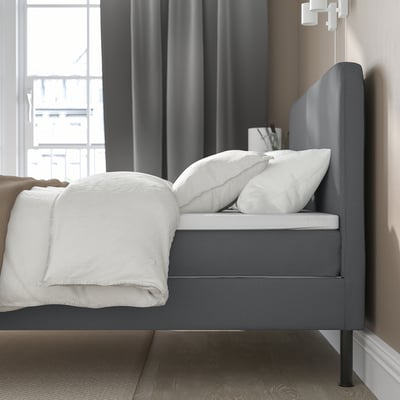 Grijs hoofdeinde bed met kussens, deken en opbergruimte onder het bed.