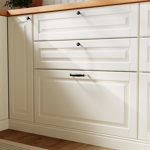 Witte keukenkast met knoppen en afgeschuinde lades op houten vloer.