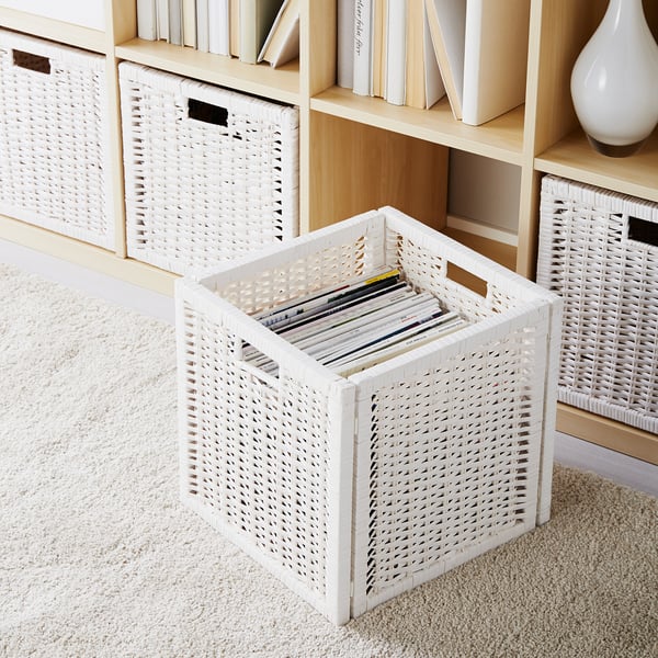 Wit gevlochten rotan opbergmanden op beige tapijt, sommige gevuld met boeken, naast een houten plank.