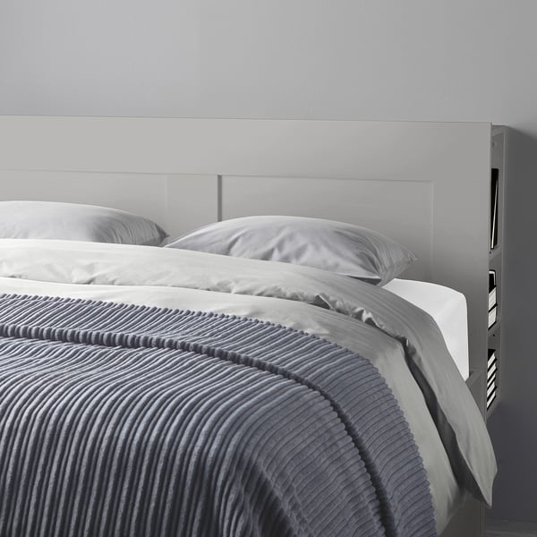 Een grijs BRIMNES bed met een hoofdeinde, met verborgen opbergruimte en verstelbare zijwanden, met een georganiseerde en gezellige slaapruimte.