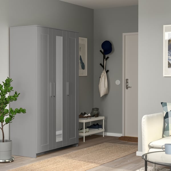 Moderne entree met grijze BRIMNES kledingkast, schoenenrek en kapstok. De kledingkast weerspiegelt de muur en voegt diepte toe. Versierd met plant en voorwerpen.