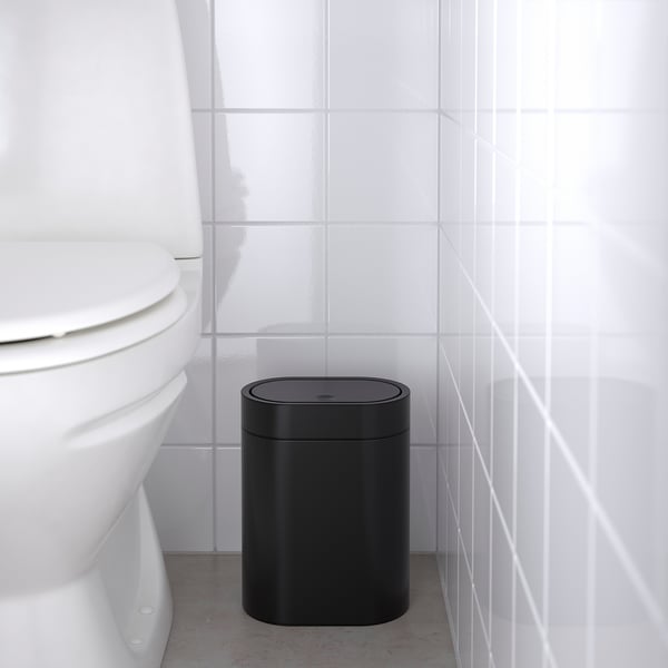 Zwarte prullenbak in de badkamer naast een wit toilet, ontworpen om in kleine ruimtes te passen.