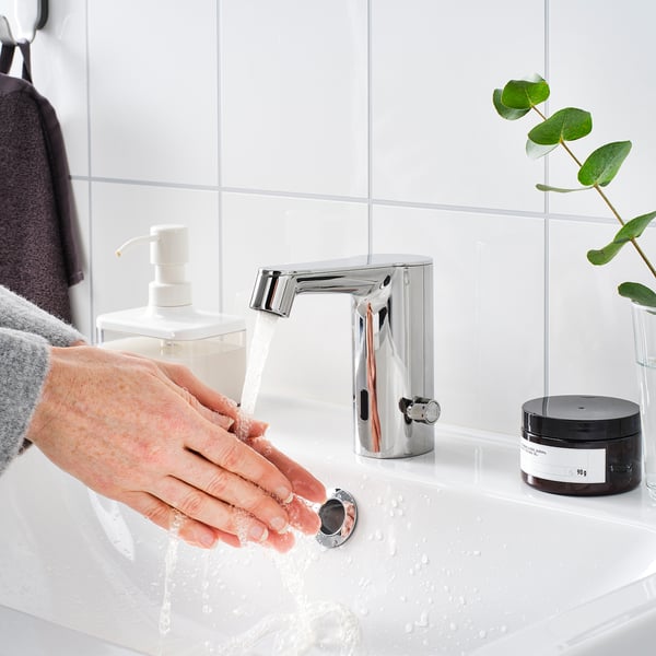 Afbeelding toont een persoon die handen wast onder een door een sensor geactiveerde contactloze kraan, die automatisch de waterstroom regelt.