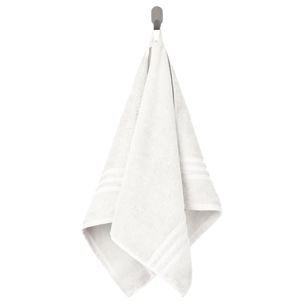 De witte handdoek BROKGLIM hangt netjes aan een haak en toont de zachte, absorberende stof met een decoratieve, geweven rand.