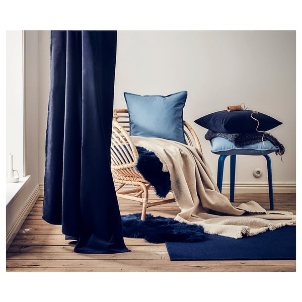 Gezellige kamer met blauwe accenten: blauwe stoel, kussens, vloerkleed en gordijnen. Natuurlijke texturen met geweven stoel, zacht textiel en houten vloer.
