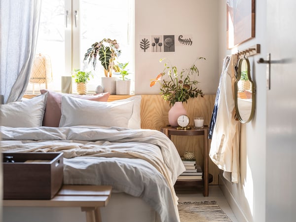 Slaapkamer met wit bed, gestreepte kussens, houten nachtkastjes, potplanten, kunst aan de muur en hangende kapstok.