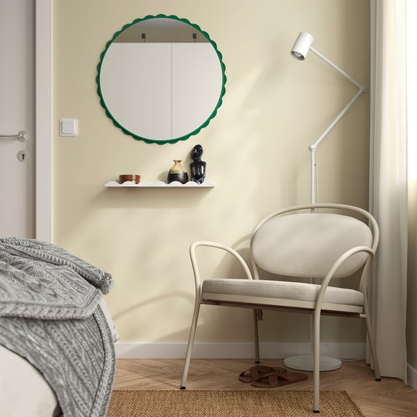 Moderne slaapkamer met spiegel, stoel en lamp. Groene ronde spiegel boven de plank, witte stoel bij het bed.