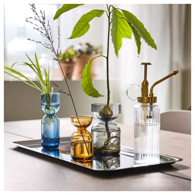 Een set van drie kleurrijke, uniek gevormde glazen vazen op een dienblad, met plantenstekken in water.